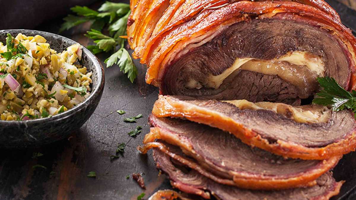 Imagem de picanha invertida recheada coberta com bacon cortada em fatias sobre a mesa