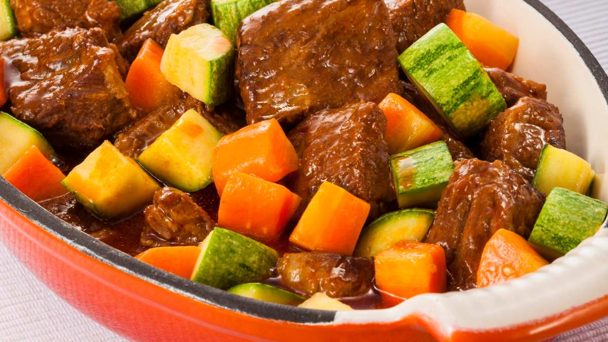 Carne de panela ensopada com legumes preparada com cubos de Costela Minga do Chef Friboi, servido em uma travessa de cor laranja.