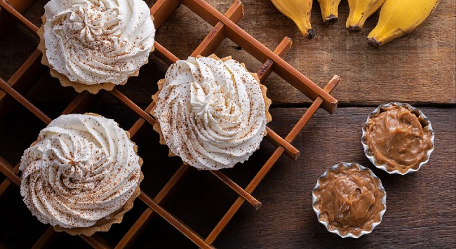 A foto mostra uma torta banoffe de banana com doce de leite servida no pote para presentear.