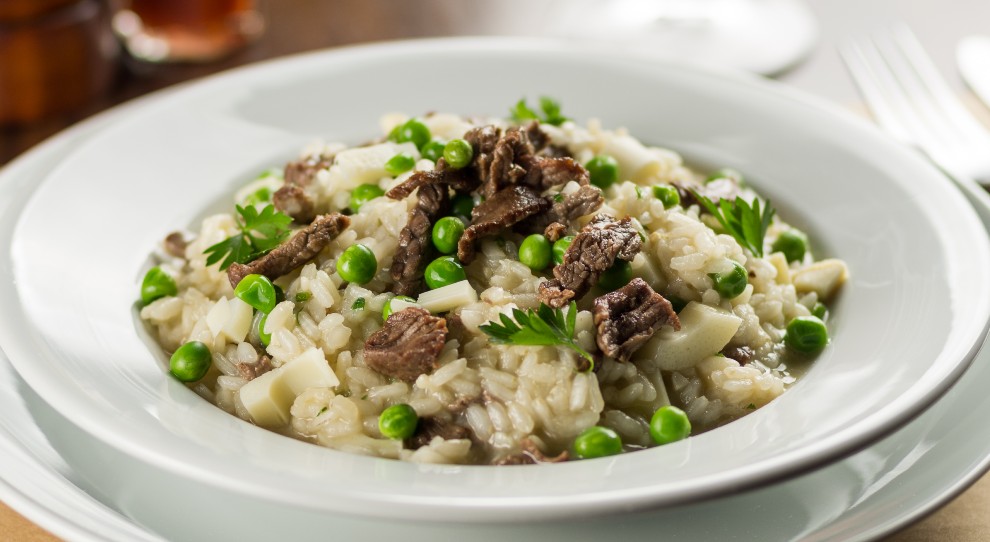 Risoto de filé mignon com ervilhas verdes servido em um prato fundo branco e redondo.