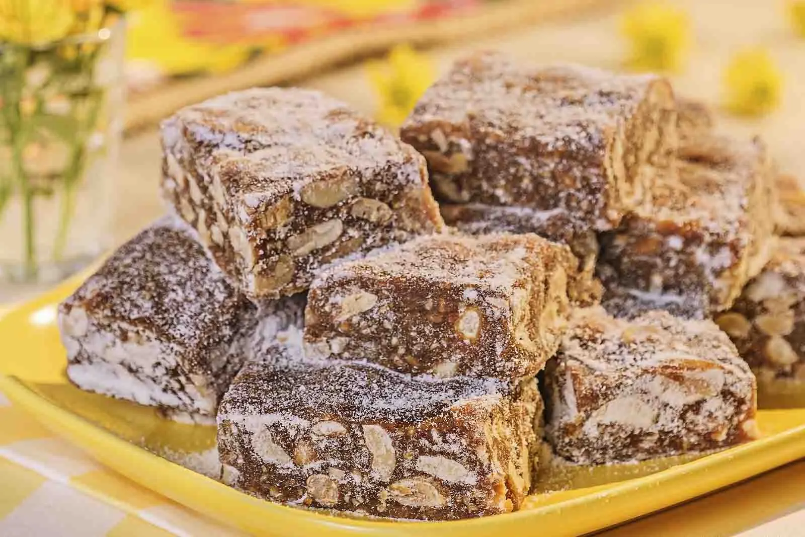 Imagem de diversos doces de amendoim, sob uma travessa retangular amarela, em cima de uma mesa de mármore 