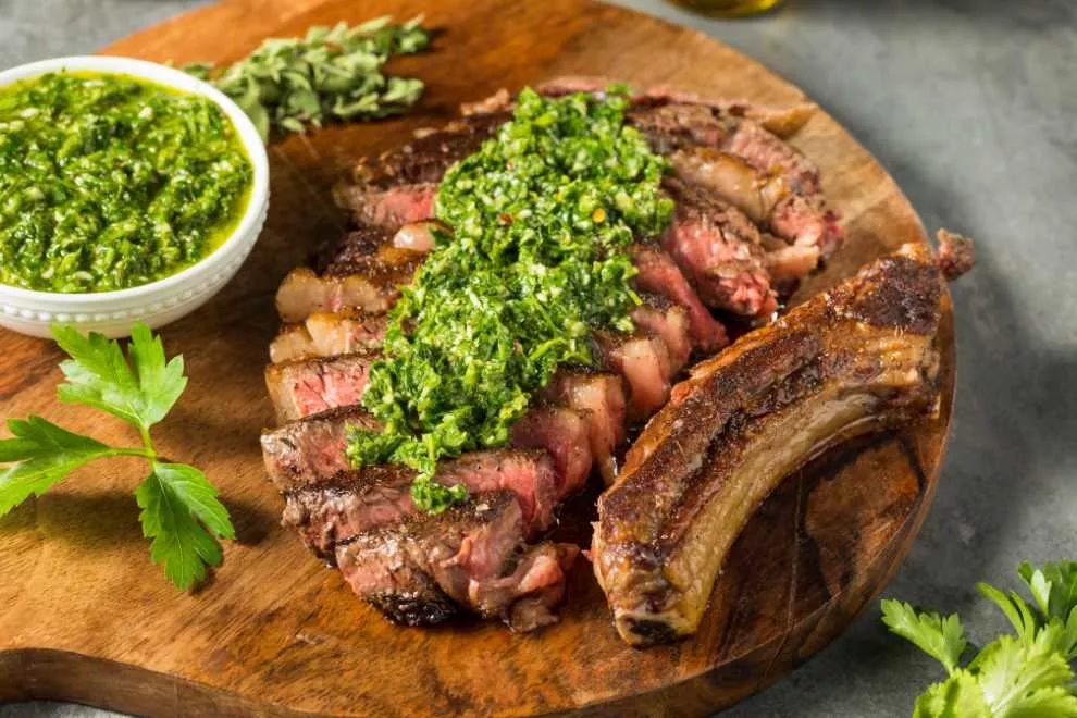 churrasco argentino com carne e molho verde encima da carne em uma tábua de madeira